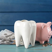 A ceramic tooth model, piggy bank, and money on a light blue wooden table